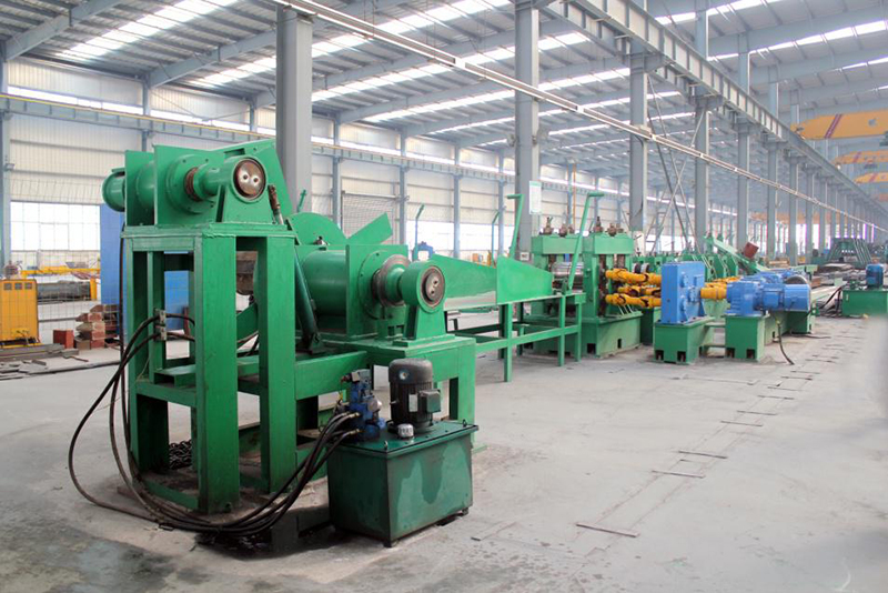 Green industrial machinery line inside a large metal warehouse, neutral tones, empty of people